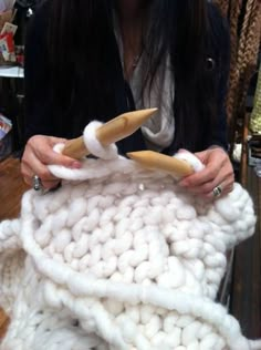 a woman is holding two knitting needles in front of a white knitted blanket with horns on it