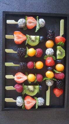 fruit skewers are arranged on sticks in a shadow box with blackberries, kiwis, oranges and raspberries