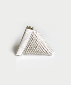 a white triangle shaped clutch bag on a white surface with a gold metal clasp in the middle