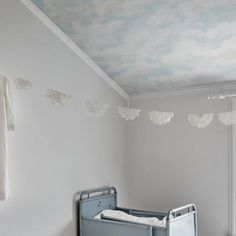 a baby's crib in the corner of a room with clouds painted on the ceiling