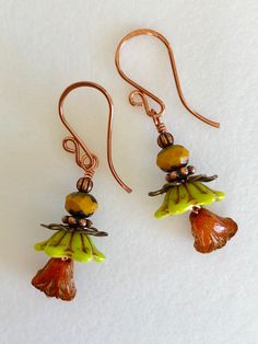 "Adorable new Czech glass premium flower earrings in chartreuse green and orange opaline with mustard yellow and copper accents. Opaque chartreuse Czech glass bellflowers with copper Picasso finish are accented with little Czech glass lilies in burnt orange opaline with metallic copper wash and mustard yellow Picasso rondelles. Wire wrapped in bright copper with copper accents. Ear wires are handmade German copper. Total drop is 1 3/4\"." Whimsical Green Czech Glass Earrings, Whimsical Yellow Jewelry With Ear Wire, Green Whimsical Flower Shaped Earrings, Whimsical Green Flower-shaped Jewelry, Orange Flower-shaped Adjustable Earrings, Nickel-free Orange Flower Earrings, Green Flower-shaped Glass Jewelry, Green Glass Flower-shaped Jewelry, Green Czech Glass Flower Earrings