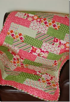 a pink and green patchwork quilt sitting on top of a brown chair next to a wall