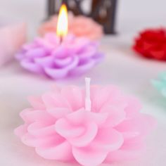 three candles with pink, purple and green flowers on them sitting on a white tablecloth