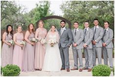 a group of people standing next to each other in front of a wooden arch and bushes