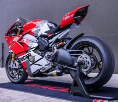 a red and white motorcycle parked on top of a black mat next to a building