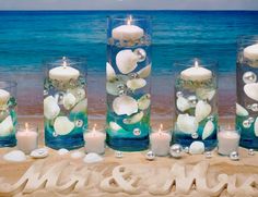 there are candles and seashells in glass vases on the beach