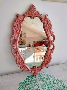 a pink mirror sitting on top of a white table next to a green doily