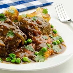 a white plate topped with meat covered in gravy next to potatoes and peas