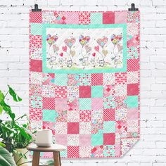 a pink and green patchwork quilt hanging on a brick wall next to a potted plant