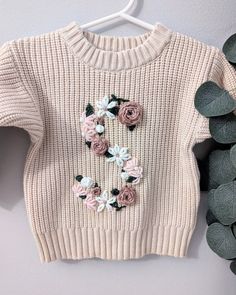 a sweater with flowers on it hanging from a hanger