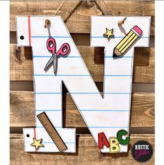 the letter n is made out of wood and has scissors, pencils, stars, and paper on it