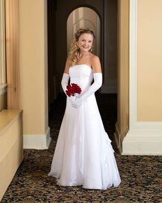 a woman in a white wedding dress holding a red rose and posing for the camera