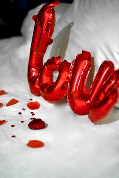 red foil balloons spelling out the word love on a white bed with petals scattered around