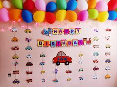 a birthday party with balloons, cars and streamers on the wall in front of it