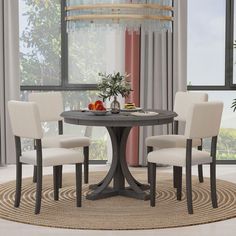 a round table with four chairs around it in front of a window and potted plant