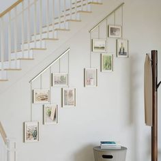 a white staircase with pictures on the wall and a trash can under it next to a stair case