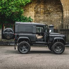 a black jeep is parked in front of a brick wall and gate with trees behind it