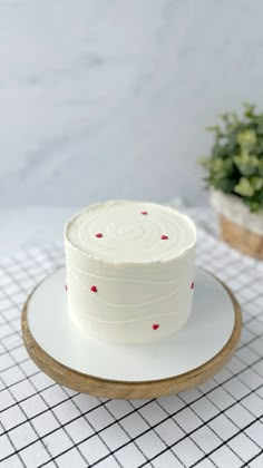 a white cake sitting on top of a plate next to a potted green plant