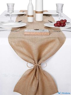 the table is set with white plates, silverware and wine bottles in burlap