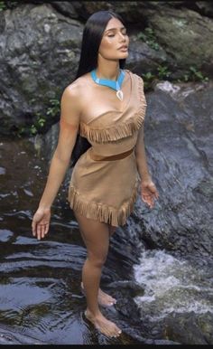 a woman standing in the water wearing a native american dress and necklace with feathers on her head