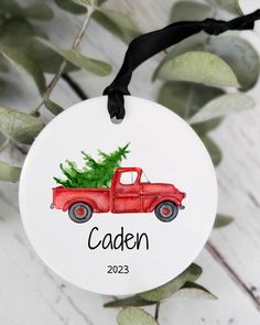 a red truck with a christmas tree on the back is hanging from a black ribbon