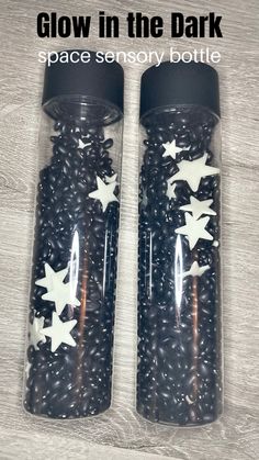 two glass jars filled with black beans and white stars on the lids that say glow in the dark space sensory bottle