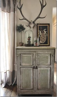 an old dresser with antlers on it in front of a painting and window sill