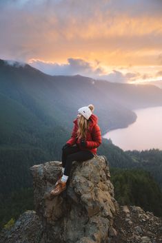 a woman sitting on top of a large rock next to a lake in the mountains