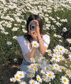 a woman taking a photo in a field of daisies