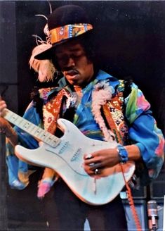 the man is playing an electric guitar with feathers on his hat and clothes, while wearing a feathered top