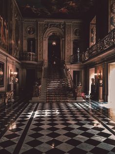 an ornate hallway with black and white checkered flooring, chandelier and staircase