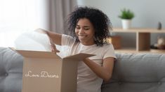 a woman sitting on a couch opening a box with the lid open and she is smiling