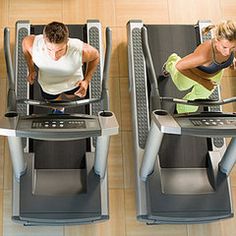 two women working out on treadmills in a gym together, looking down at the floor