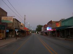 an empty street with buildings and signs on the side walk at dusk in a small town