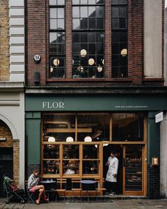 two people sitting on chairs in front of a store with lots of windows and doors