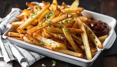 french fries with ketchup and parsley in a white dish on a wooden table