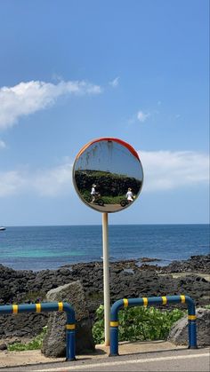 there is a mirror on the side of the road by the ocean and people in it