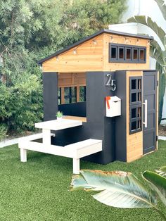 a small house with a picnic table in the grass next to some trees and bushes