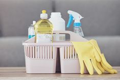 cleaning supplies and gloves sitting in a basket on a wooden table next to a couch