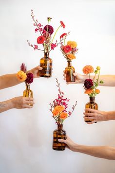 four people holding vases with flowers in them and reaching for each other's hand