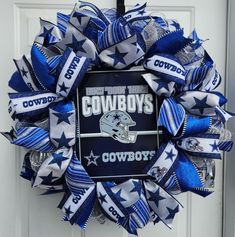 a wreath with the word cowboys on it is hanging from a white door and decorated with blue and silver ribbons