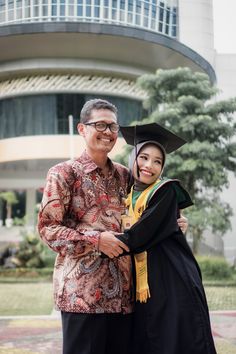 a man and woman in graduation gowns posing for a photo outside an office building