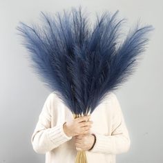 a woman holding a bunch of blue feathers on her head and wearing a white sweater