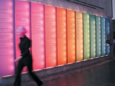 a woman walking past a colorful wall with many books on it's display case