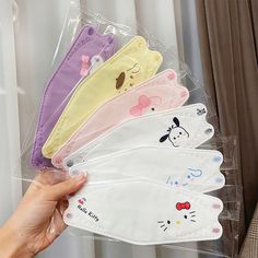 five pairs of face masks with cartoon characters on them in plastic bags, one being held by a woman's hand