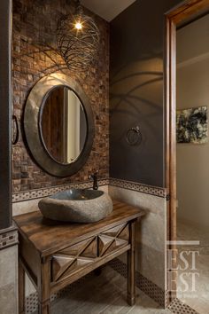 a bathroom with a wooden table and round mirror on the wall, along with a stone sink