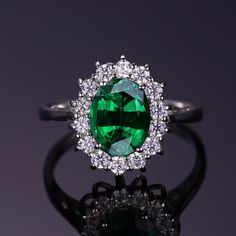 an oval cut green gemstone surrounded by white diamonds on a black ring with reflection