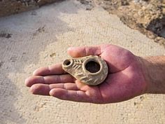 a hand holding a small clay object in it's right hand on the sand