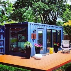 a large blue container house sitting on top of a wooden deck next to a tree