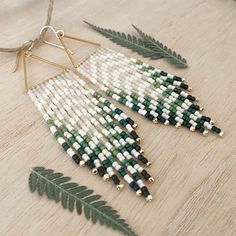 a pair of earrings with beads and leaves on a wooden table next to a plant